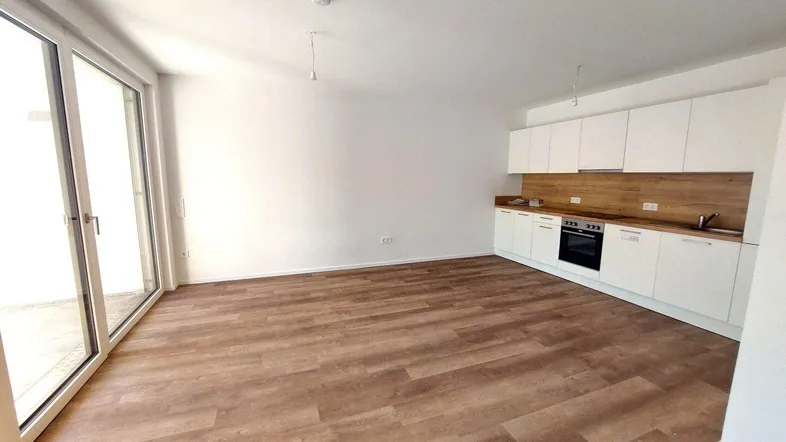 Heller Wohn- und Essbereich mit integrierter Küchenzeile, Laminatboden und Zugang zum Balkon.