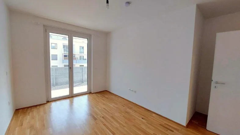 Helles Zimmer mit Holzboden und Zugang zu einem Balkon, ideal für individuelle Gestaltung.