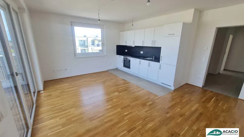 Heller Wohnbereich mit Parkettboden, integrierter Küchenzeile und Zugang zum Balkon.