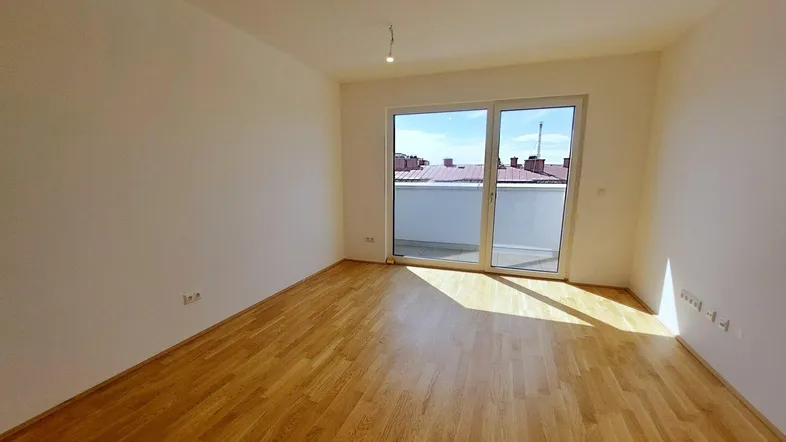 Helles Zimmer mit Holzboden und Zugang zu einem Balkon oder einer Terrasse.