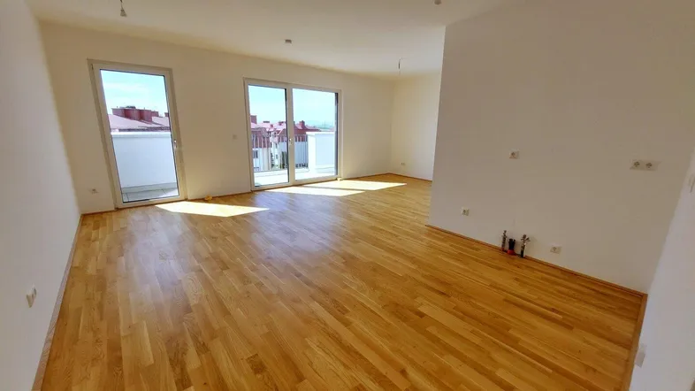 Helles, leeres Wohnzimmer mit neuem Parkettboden und Zugang zu einem Balkon.