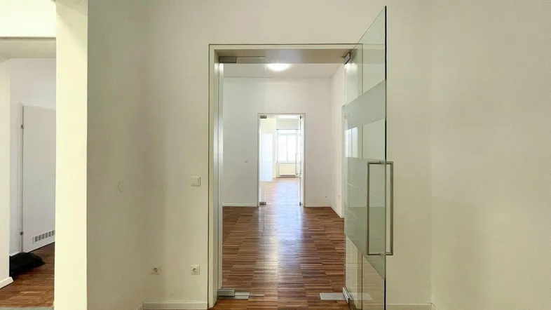 Heller Flur mit Holzboden und moderner Glastür, die zu weiteren Räumen führt.
