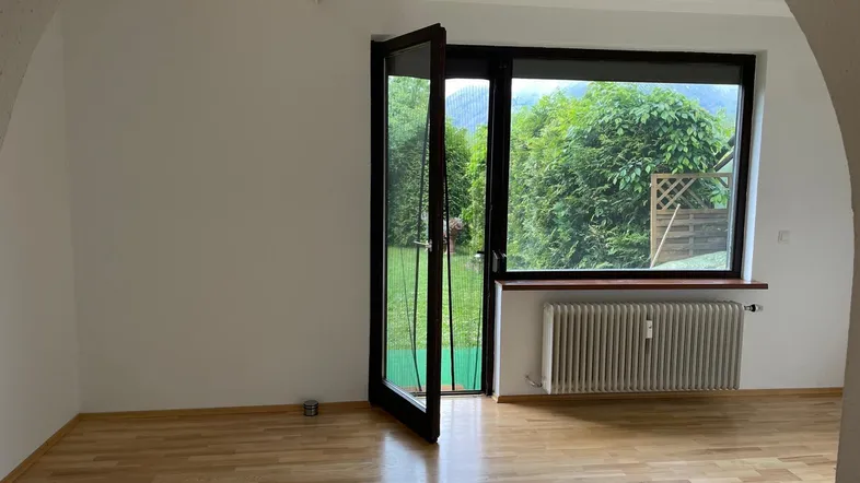Heller Wohnraum mit Holzboden, großen Fenstern und Zugang zu einer grünen Außenfläche.