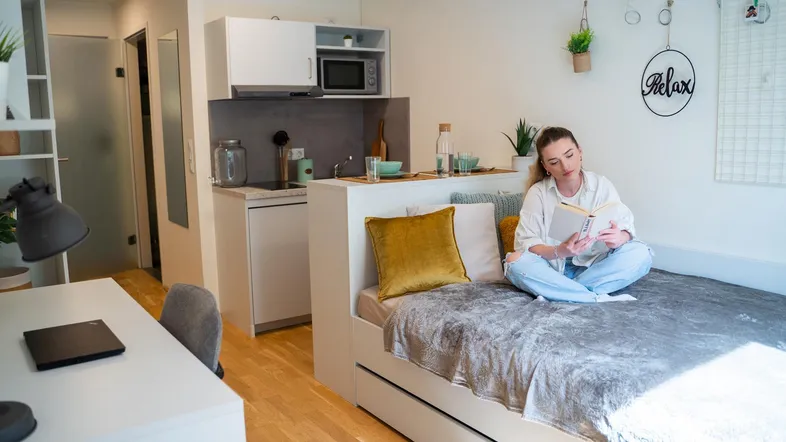 Gemütliches Studio-Apartment mit Bett, integrierter Küchenzeile und hellem Arbeitsbereich.