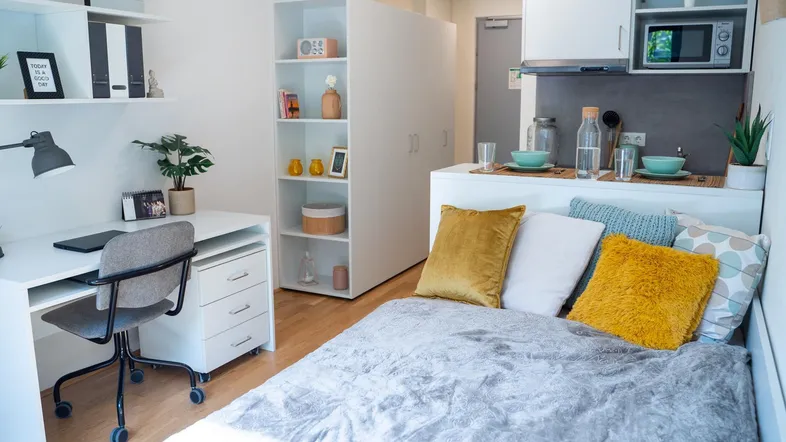 Helles Studio-Apartment mit Bett, Schreibtisch und integrierter Küchenzeile, ideal für Studenten.