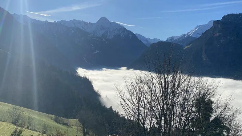 Sonniger Gartenbereich mit Sitzgelegenheiten und atemberaubendem Bergblick über ein Nebelmeer.