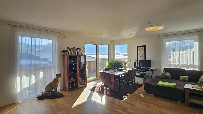 Helles Wohn- und Esszimmer mit Holzboden, großen Fenstern und Zugang zum Außenbereich.