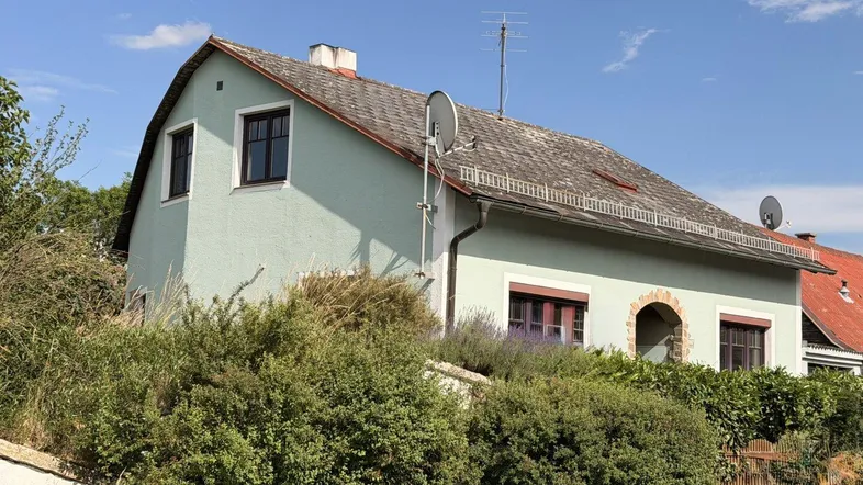 Traditionelles Einfamilienhaus mit hellgrüner Fassade und Satteldach unter blauem Himmel.