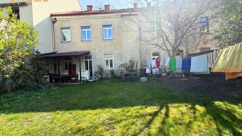 Hinterhof mit großem Rasenbereich, überdachter Terrasse und Wäscheleine, umgeben von Bäumen.