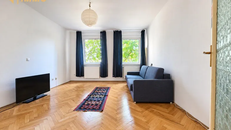Helles Wohnzimmer mit Fischgrätparkettboden, einem Sofa und Blick ins Grüne durch die Fenster.
