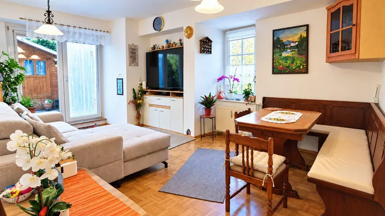 Gemütlicher Wohn-Essbereich mit beigem Sofa, Holzboden und Zugang zum Garten.