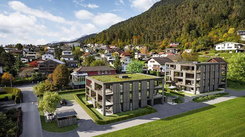Moderne Wohngebäude in grüner Umgebung mit Bergblick und Flachdächern, eingebettet in die Natur.