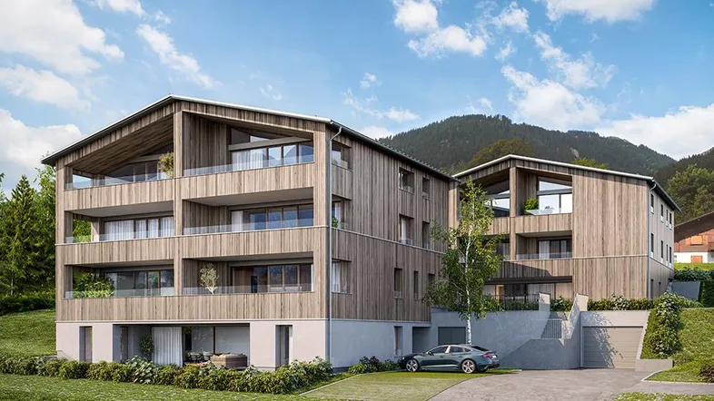 Modernes Mehrfamilienhaus mit Holzfassade, Balkonen und Tiefgaragenzufahrt vor alpiner Bergkulisse.