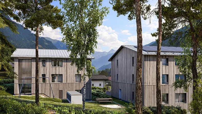 Zwei moderne Holzgebäude in alpiner Landschaft mit Bergblick und Photovoltaikanlage auf dem Dach.
