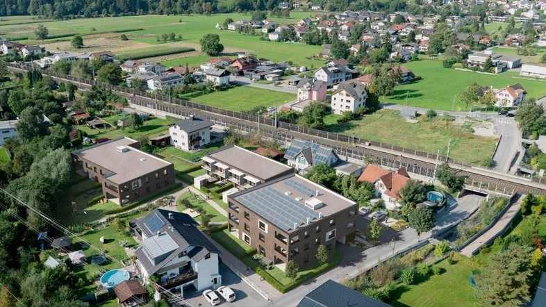 Luftaufnahme einer modernen Wohnanlage mit mehreren Gebäuden, umgeben von grüner Landschaft und Bergen.
