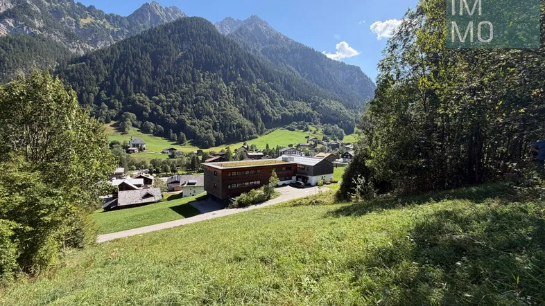 Panoramablick auf die umliegende Berglandschaft mit grünen Wiesen und vereinzelten Gebäuden im Tal.