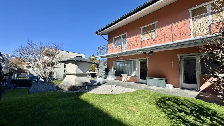 Gepflegter Gartenbereich mit Rasenfläche, Steinterrasse und Außengrill hinter dem Haus.