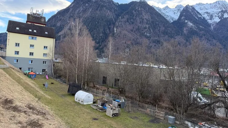 Blick auf das Gebäude mit Gartenbereich, Spielplatz und majestätischem Bergpanorama im Hintergrund.