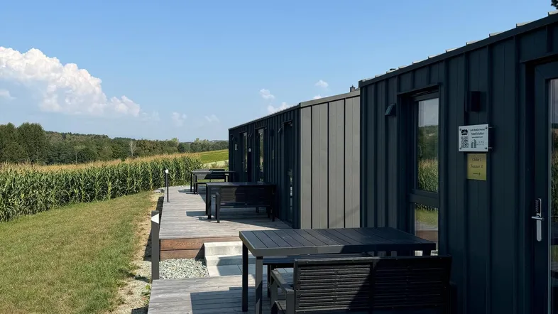 Mehrere moderne Modulhäuser mit Holzterrassen und Sitzgelegenheiten, umgeben von grüner Landschaft und Feldern.