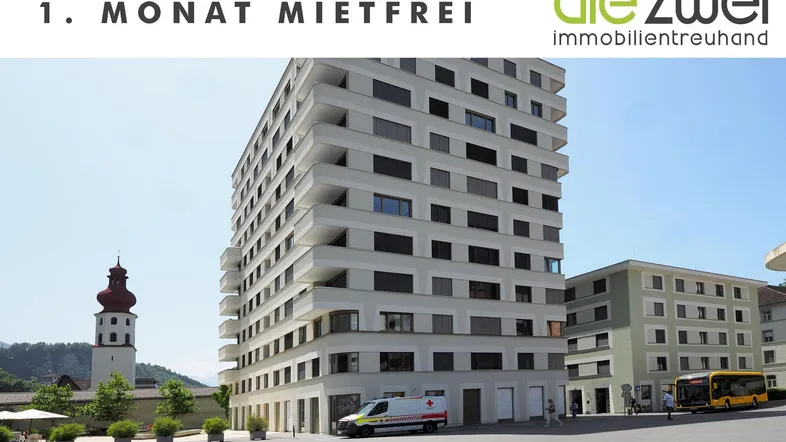 Modernes Mehrfamilienhaus mit Balkonen und Blick auf einen Kirchturm in städtischer Umgebung.