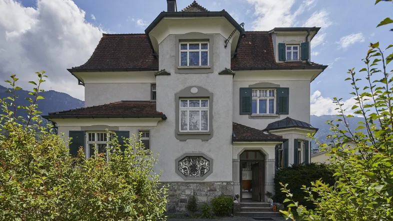 Repräsentative Fassade einer historischen Villa mit traditionellen Fensterläden und gepflegtem Vorgarten.