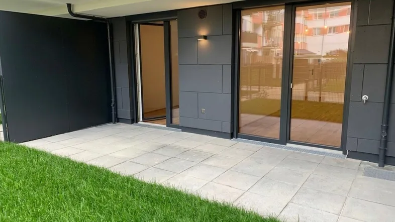 Moderne Terrasse mit Steinplatten und direktem Zugang zum Gartenbereich eines Neubaus.