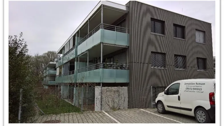 Modernes Mehrfamilienhaus mit dunkler Fassade, Balkonen und Parkplätzen.