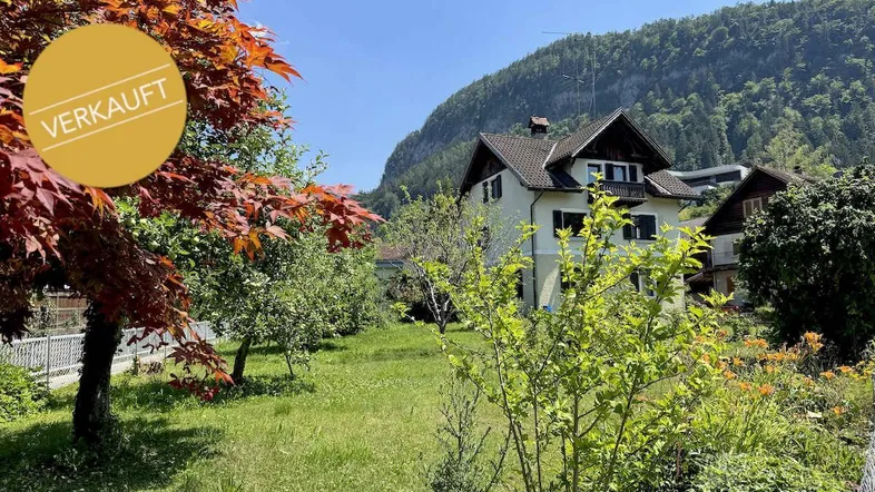 Charmantes Haus mit gepflegtem Garten und herrlichem Bergblick unter blauem Himmel.