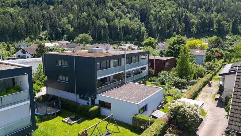 Moderne Wohnanlage mit Flachdach, Balkonen und einem gepflegten Garten mit Spielgeräten, umgeben von viel Grün.