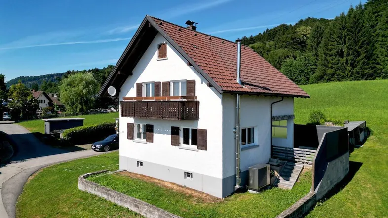 Freistehendes Haus mit Balkonen und Satteldach, umgeben von grünen Wiesen.