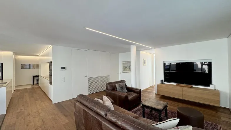 Geräumiges Wohnzimmer mit Holzboden, bequemen Ledersofas und integrierter Deckenbeleuchtung.