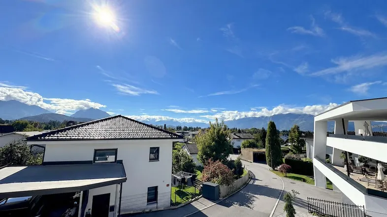 Sonniger Ausblick auf die umliegende Wohngegend und die majestätische Berglandschaft unter blauem Himmel.