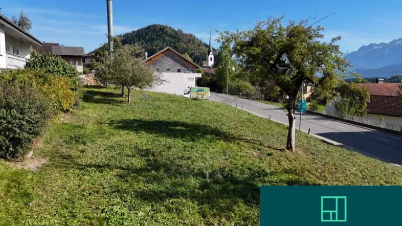 Grünfläche mit Blick auf die umliegende Landschaft und Berge, neben einer Straße gelegen.