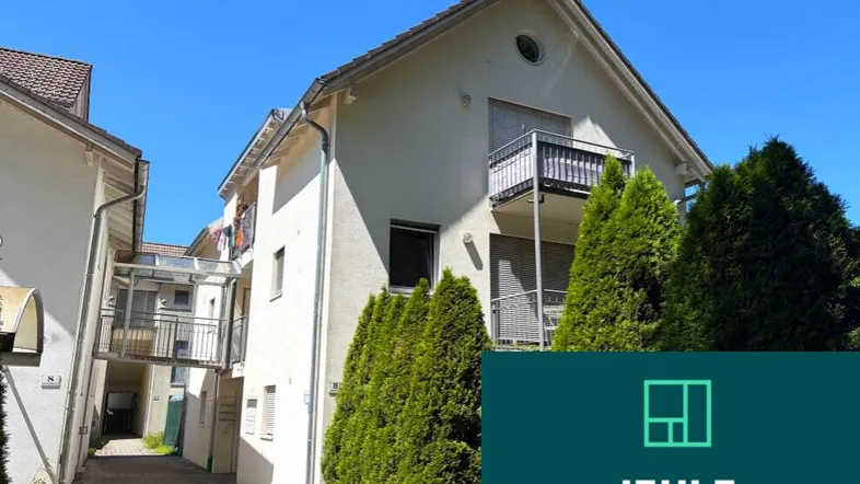 Mehrfamilienhaus mit mehreren Balkonen und gepflegten Büschen unter blauem Himmel.