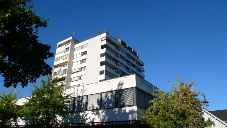 Mehrstöckiges Wohngebäude mit weißen Fassaden und zahlreichen Balkonen unter blauem Himmel.