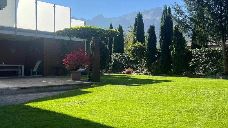 Weitläufiger Gartenbereich mit hohen Bäumen, gepflegtem Rasen und beeindruckendem Bergblick.