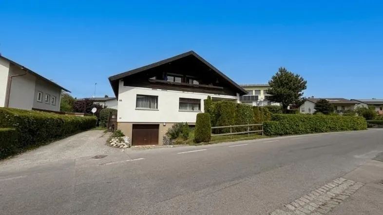 Einfamilienhaus mit Satteldach, Garage im Untergeschoss und gepflegter Hecke an der Straße.