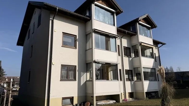 Mehrfamilienhaus mit mehreren Etagen, Balkonen und großen Fenstern unter blauem Himmel.
