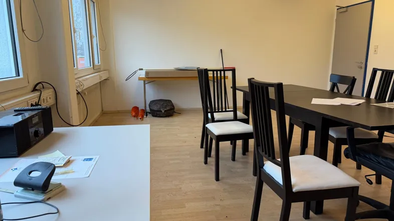 Heller Büroraum mit großen Fenstern, Holzboden und einem Besprechungstisch, der viel Tageslicht hereinlässt.