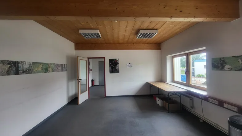Geräumiges Büro mit Holzbalkendecke, großen Fenstern und viel Tageslicht, ideal für produktives Arbeiten.
