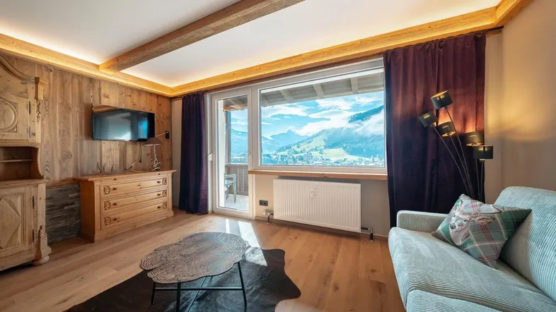 Helles Wohnzimmer im alpinen Stil mit Holzwänden, Sofa und großem Fenster mit beeindruckendem Bergblick.