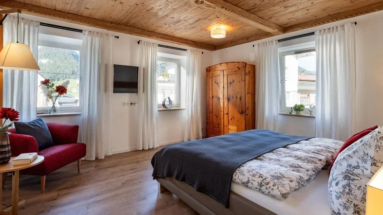 Gemütliches Schlafzimmer mit Holzbalkendecke, Parkettboden und einem roten Sofa, hell und einladend.