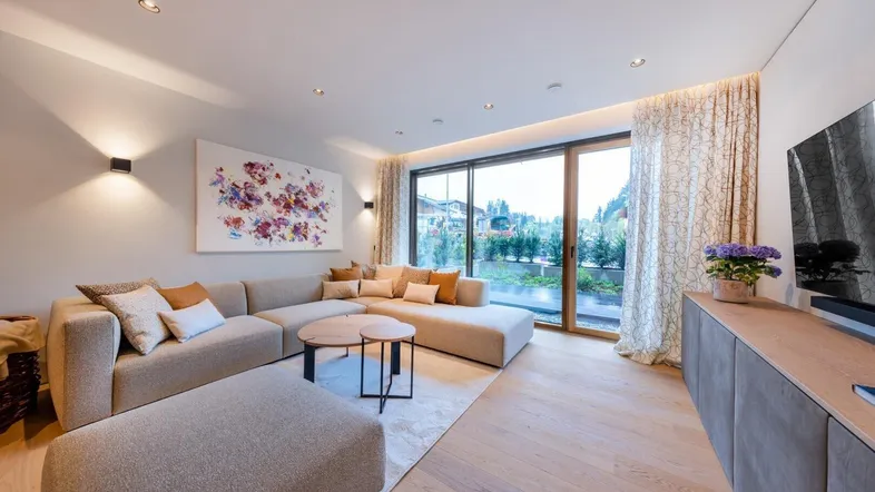 Helles Wohnzimmer mit großem Sofa, Holzboden und Zugang zu einer Terrasse mit Bergblick.