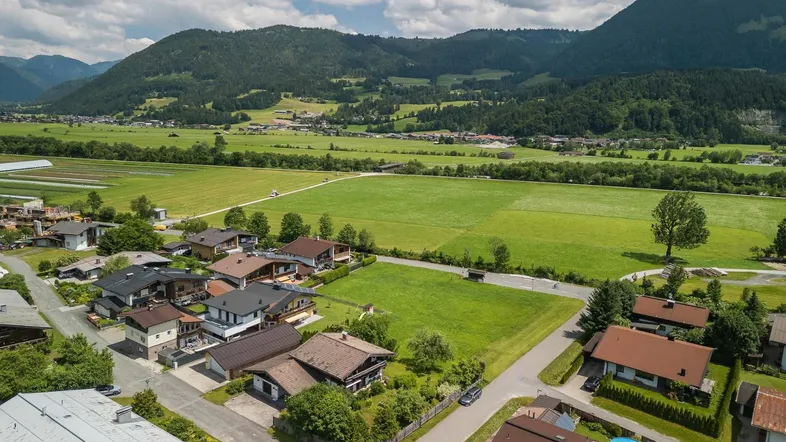 Luftaufnahme einer ländlichen Wohnsiedlung mit weiten Feldern und majestätischen Bergen im Hintergrund.
