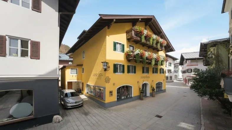 Gelbes Gebäude im traditionellen Stil mit Blumenkästen an den Balkonen in einer belebten Gasse.