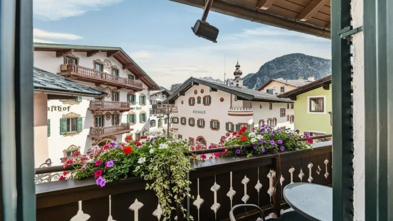 Gemütlicher Balkon mit bunten Blumenkästen und malerischem Blick auf die umliegenden Alpenhäuser und Berge.