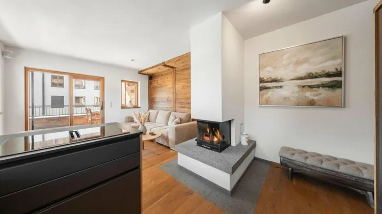 Helles Wohnzimmer mit Holzboden, modernem Kamin und Zugang zu einem Balkon.