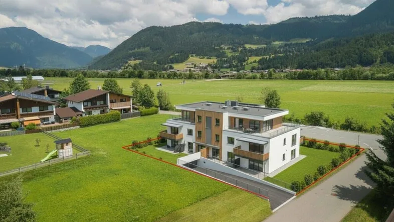 Moderne Wohnanlage mit Flachdach und Balkonen, umgeben von grünen Wiesen und Bergen.