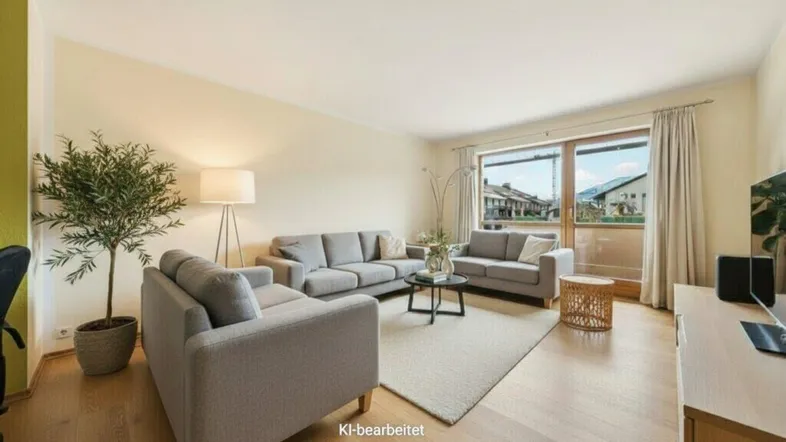 Helles Wohnzimmer mit drei grauen Sofas, Holzboden und Zugang zum Balkon.