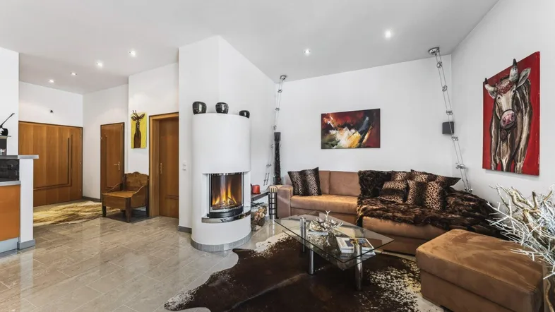Gemütliches Wohnzimmer mit Kamin, bequemer Couch und dekorativem Kuhfell-Teppich auf Fliesenboden.